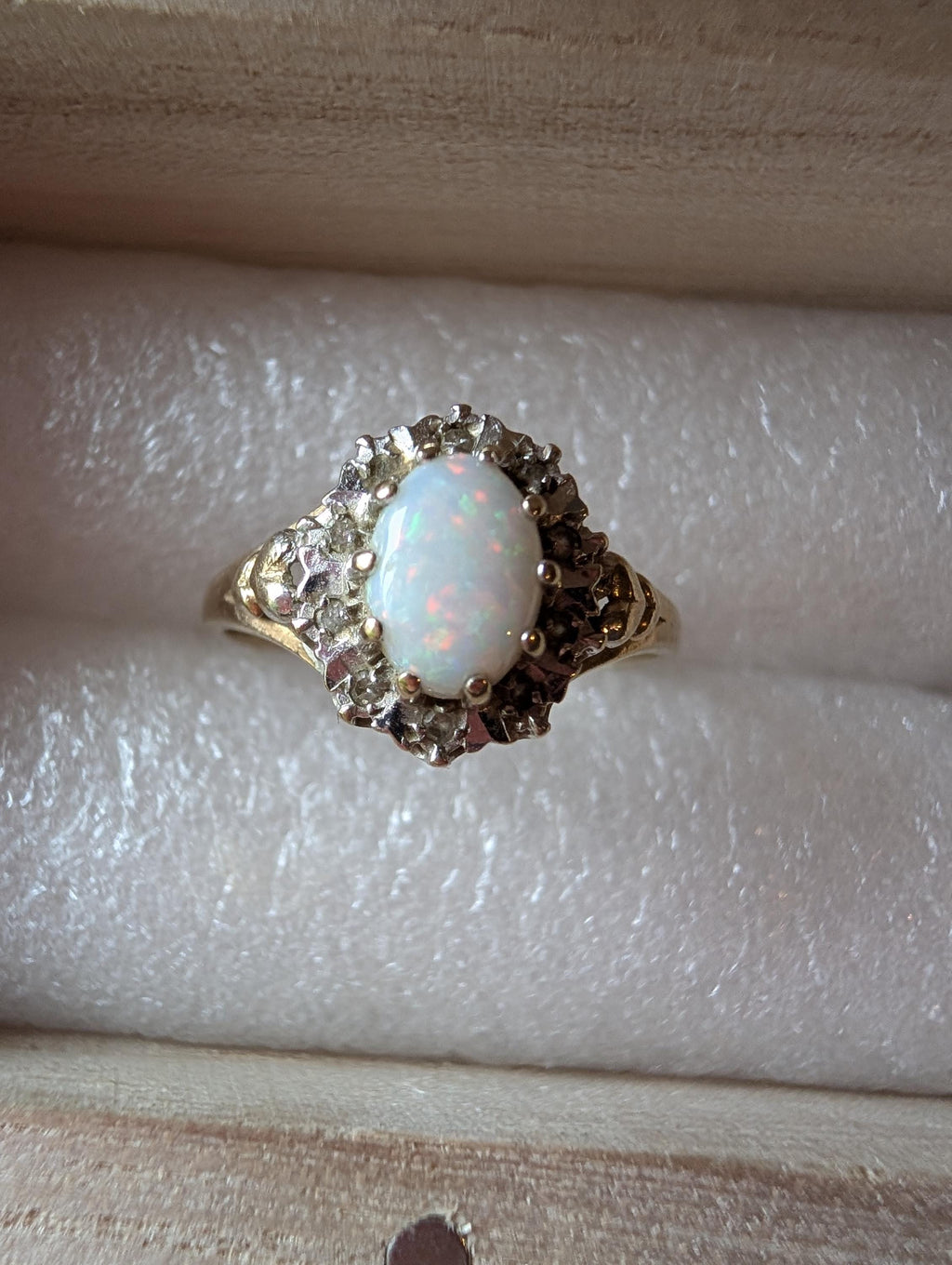A gold ring with an oval opal gemstone, encircled by diamonds. The ring has an intricate, decorative setting, giving it a vintage look. The opal is milky white with a hint of iridescence, typical of opals. __etsy:7901972023