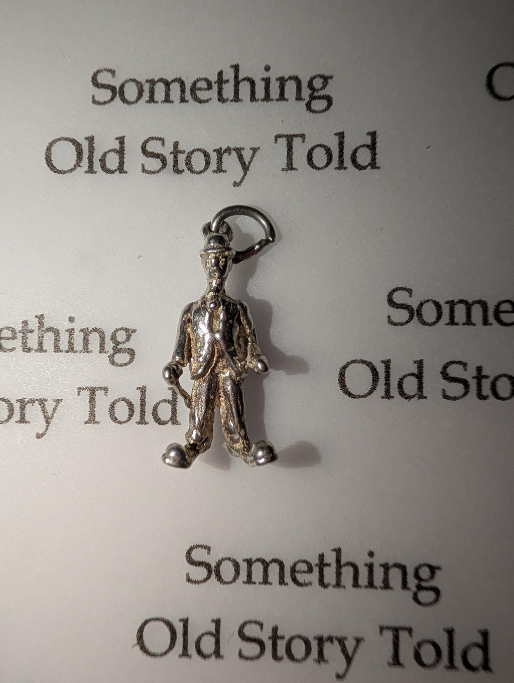 A small, silver-coloured charm depicting a man in a suit and hat, holding a cane. The charm is attached to a small loop. The background features the text "Something Old Story Told". __etsy:7855648211