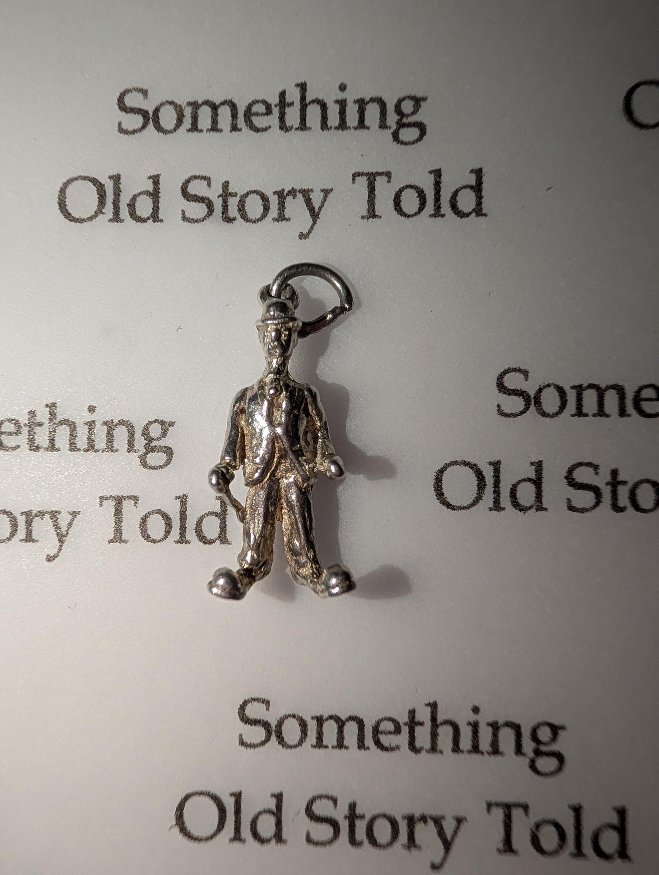 A small, silver-coloured charm depicting a man in a suit and hat, holding a cane. The charm is attached to a small loop. The background features the text "Something Old Story Told". __etsy:7855648211