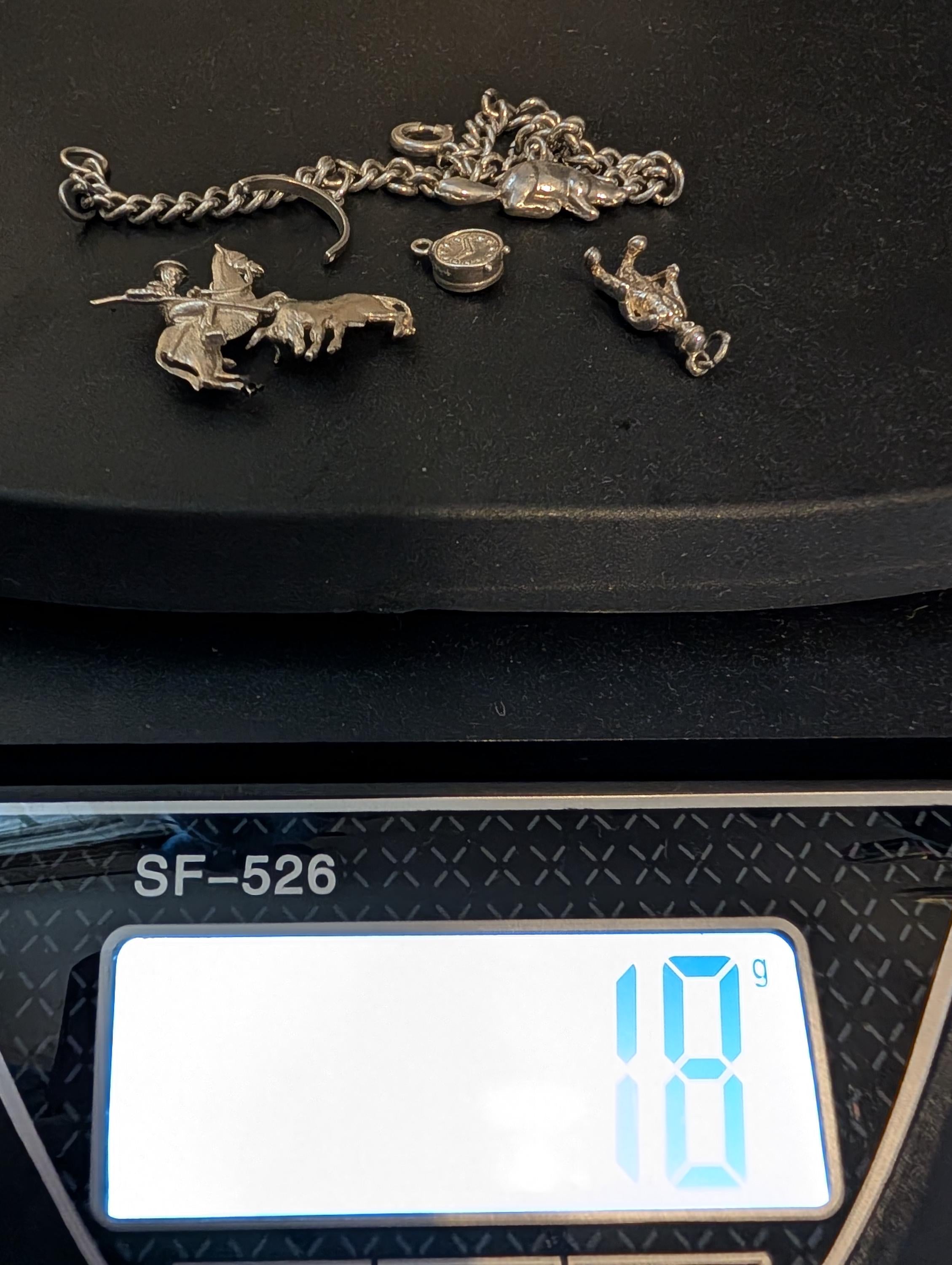 A selection of silver charms and a chain are presented on a black surface. The charms feature a rider on a horse, a bull, a crown, and a small round charm. The digital scale shows a weight of 18 grams. __etsy:7807707326