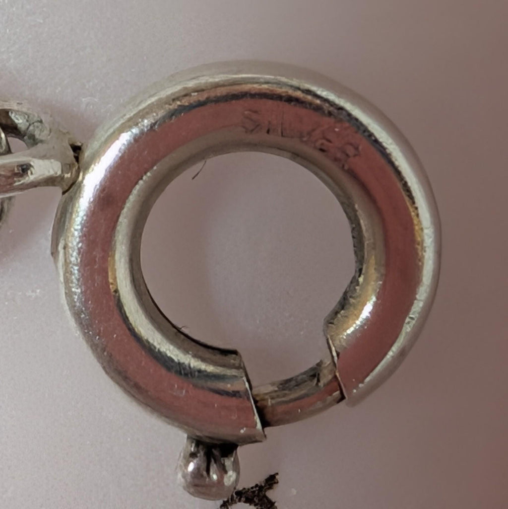 A close-up shot of a silver clasp, featuring the word "SILVER" stamped inside. The circular clasp has a hinged opening and a small ball detail. The background is a soft, neutral colour. __etsy:7855648171