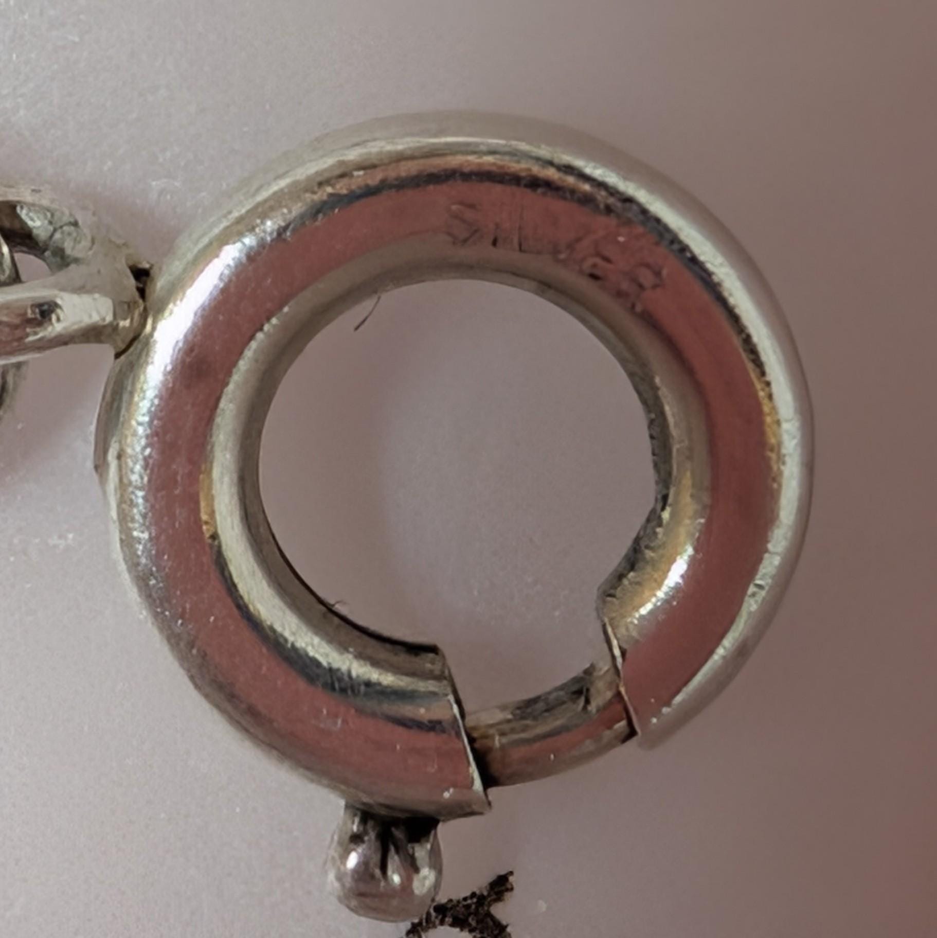 A close-up shot of a silver clasp, featuring the word "SILVER" stamped inside. The circular clasp has a hinged opening and a small ball detail. The background is a soft, neutral colour. __etsy:7855648171