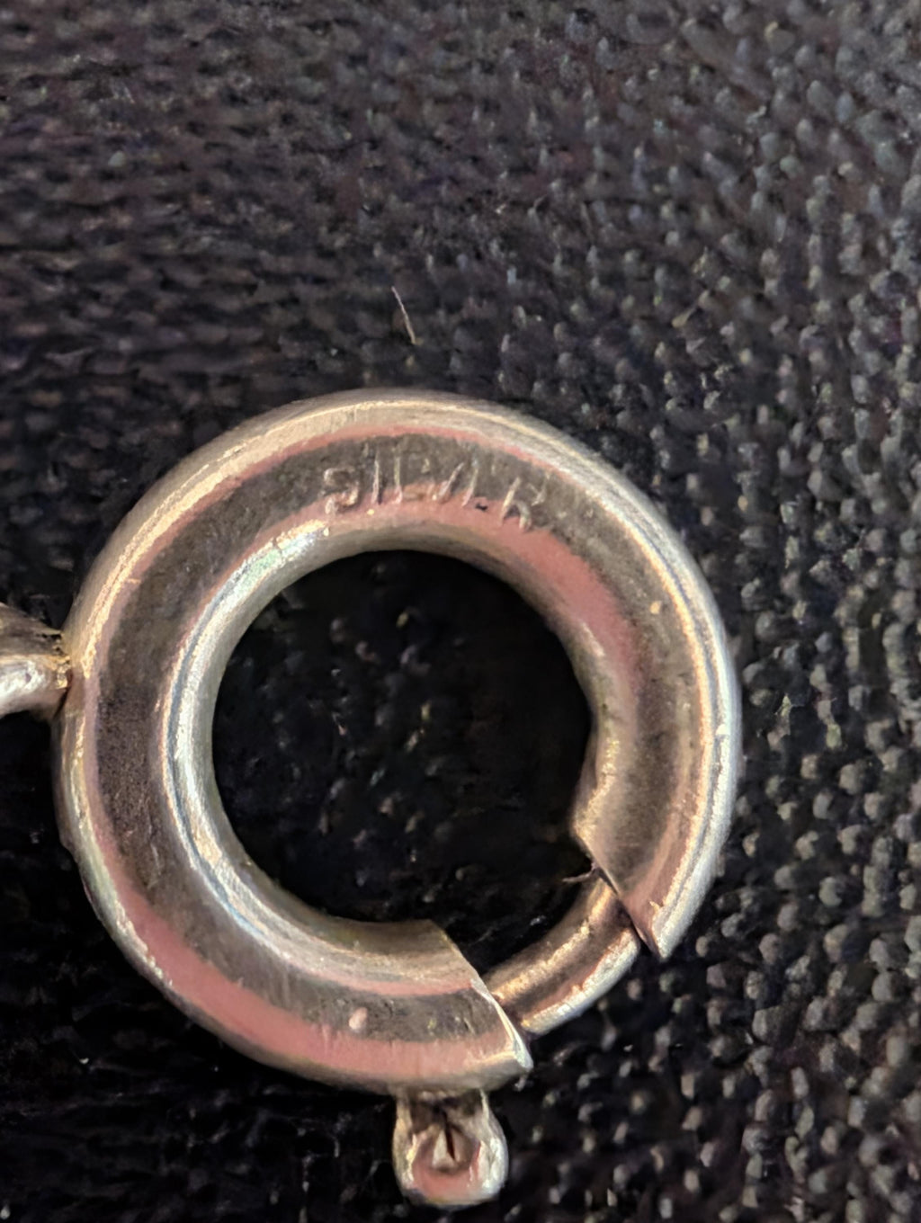 Close-up of a silver spring ring clasp. The word "SILVER" is stamped on the ring. The clasp is open, revealing the mechanism. The background is a dark, textured surface. __etsy:7855648249