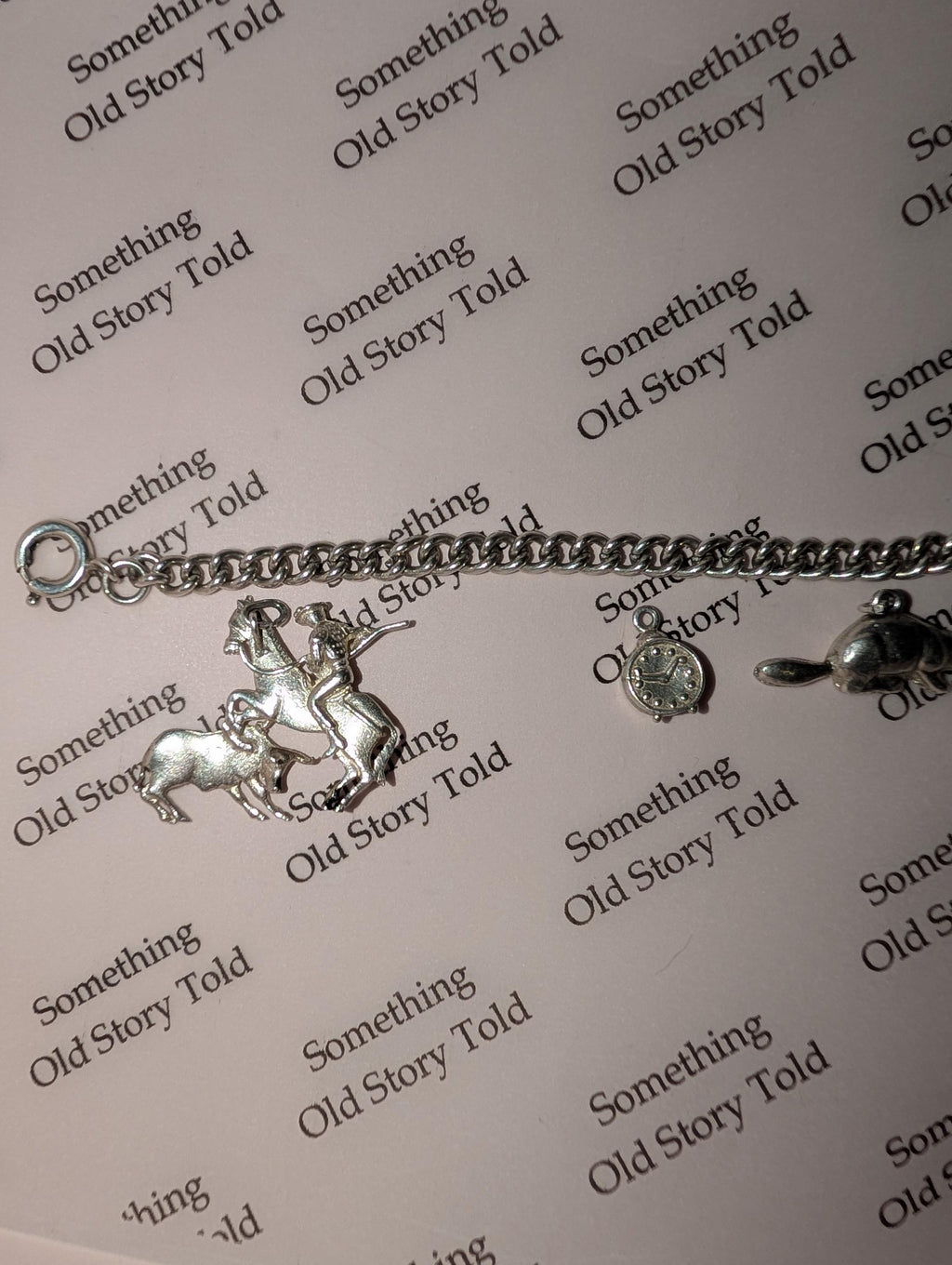 A silver charm bracelet featuring a horse and rider, a clock, and a turtle charm. The bracelet is displayed on a light pink surface with the words "Something Old Story Told" printed repeatedly. __etsy:7855648203