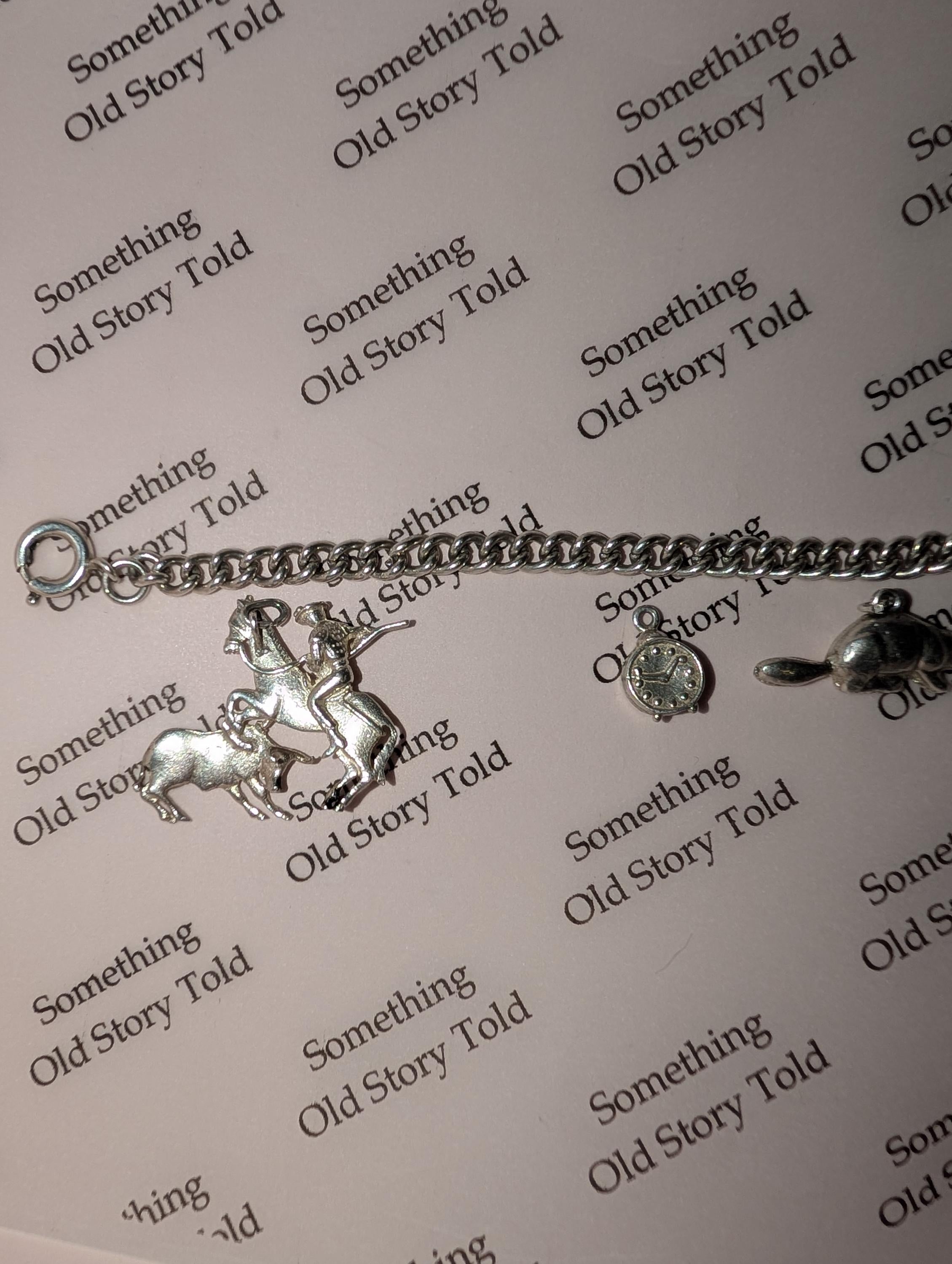 A silver charm bracelet featuring a horse and rider, a clock, and a turtle charm. The bracelet is displayed on a light pink surface with the words "Something Old Story Told" printed repeatedly. __etsy:7855648203