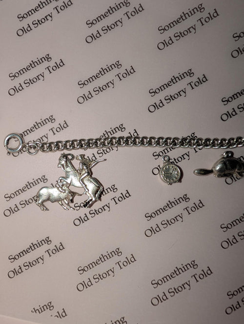 A silver charm bracelet featuring a horse and rider, a clock, and a turtle charm. The bracelet is displayed on a light pink surface with the words "Something Old Story Told" printed repeatedly. __etsy:7855648203