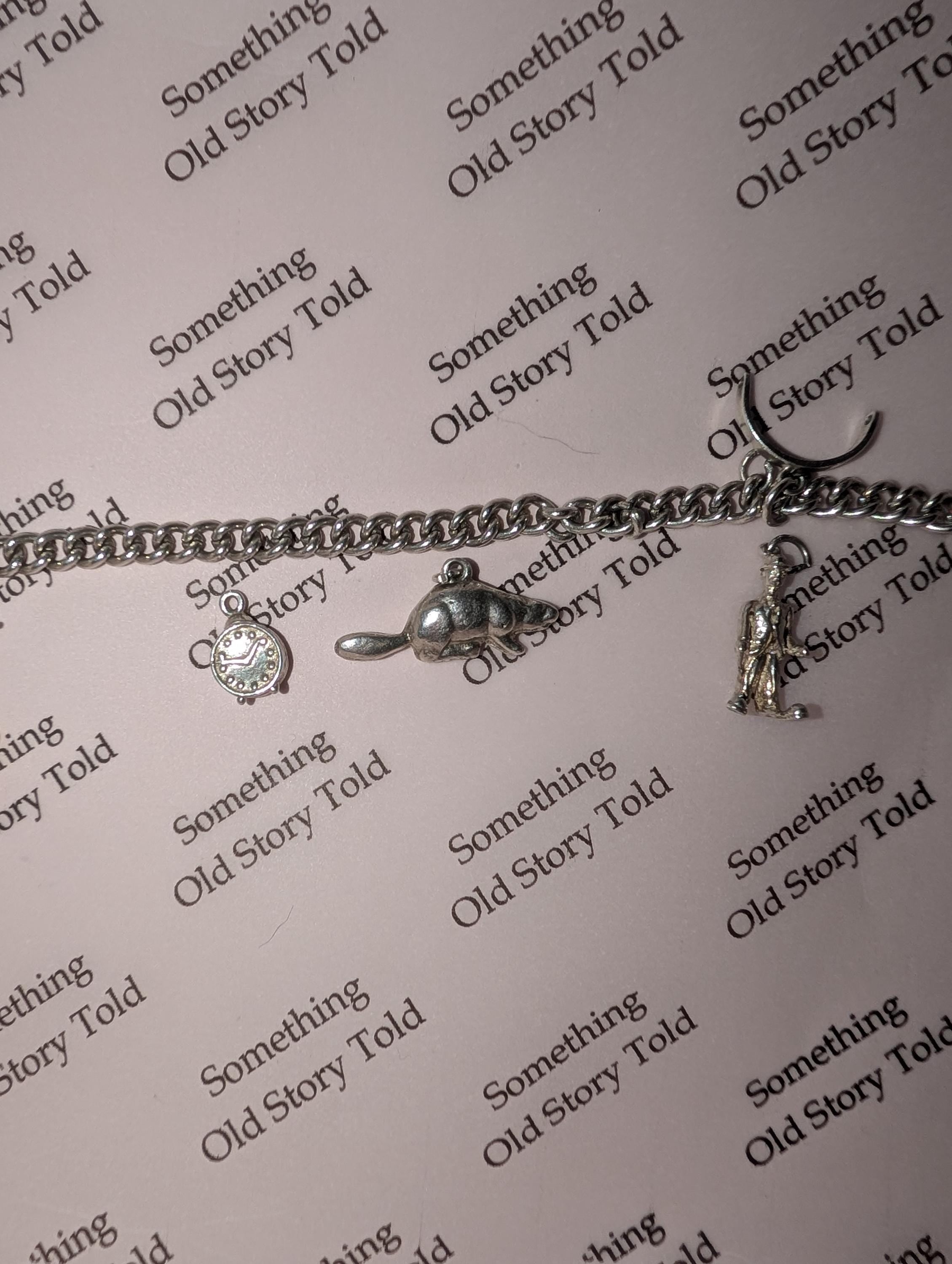 A silver charm bracelet featuring a clock, a beaver, and a figure charm. The bracelet is displayed on a pink background with the repeated text "Something Old Story Told". __etsy:7807707272